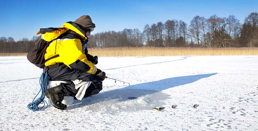 Man with ice fishing gear on the ice fishing in a whole in the ice